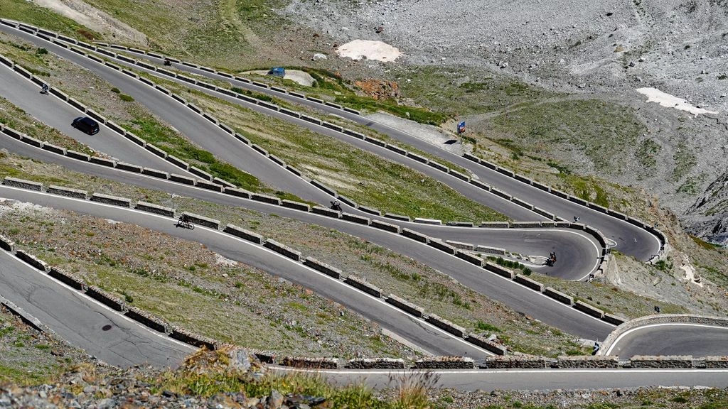 The serpentine road of Passo dello Stelvio descending into a misty alpine valley at dawn